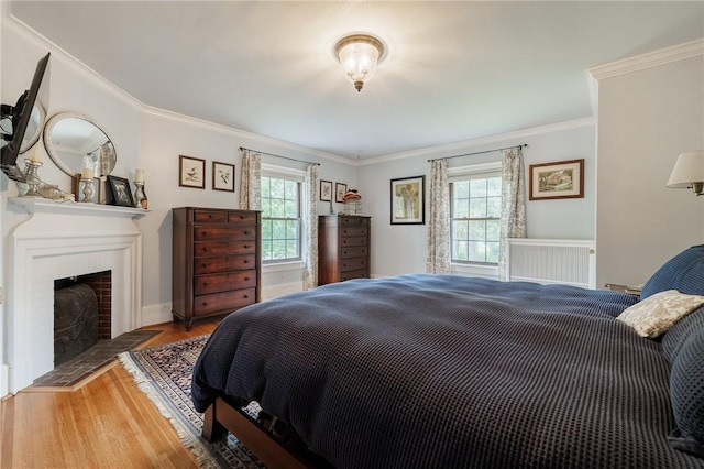 bedroom featuring wood finished floors, ornamental molding, a fireplace with flush hearth, and baseboards