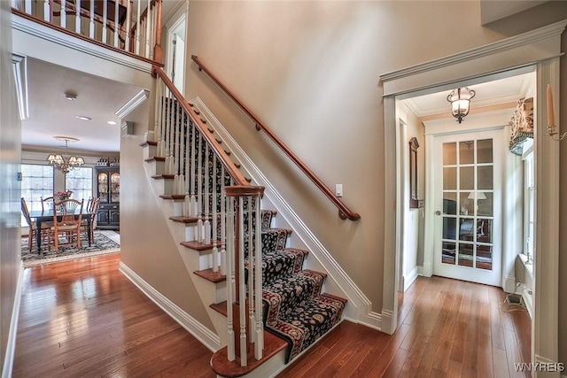 staircase with crown molding, a chandelier, wood-type flooring, and baseboards