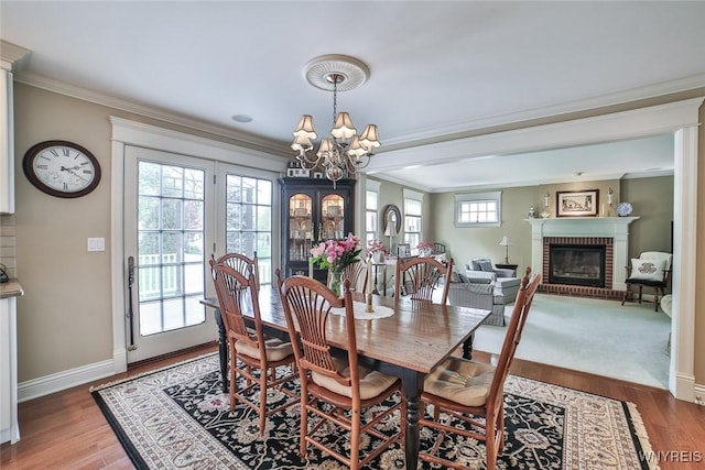 dining room featuring a chandelier, ornamental molding, a fireplace, wood finished floors, and baseboards