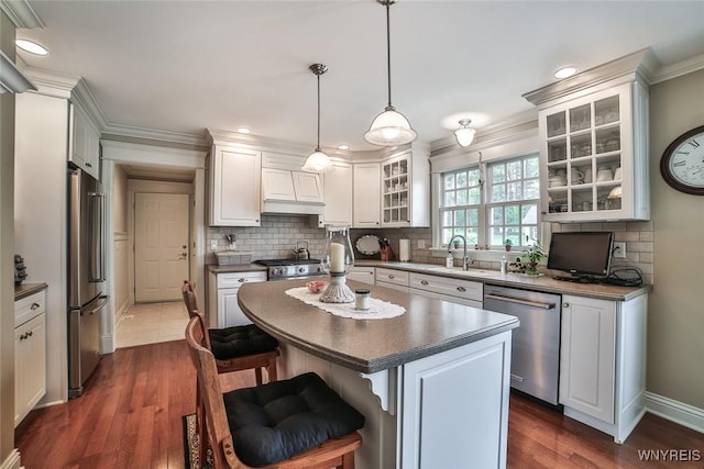 kitchen featuring appliances with stainless steel finishes, dark countertops, a breakfast bar area, a sink, and ornamental molding