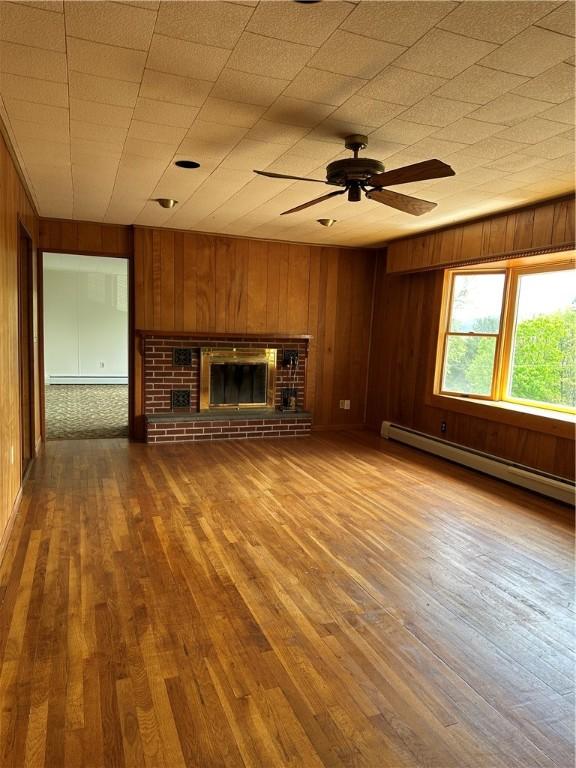 22 Suncrest Ter, Oneonta-City, NY 13820 - unfurnished living room with a baseboard heating unit, ceiling fan, a fireplace, wood walls, and wood finished floors