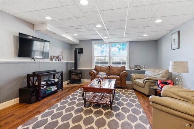 living area with wood finished floors, a wood stove, baseboards, a drop ceiling, and recessed lighting