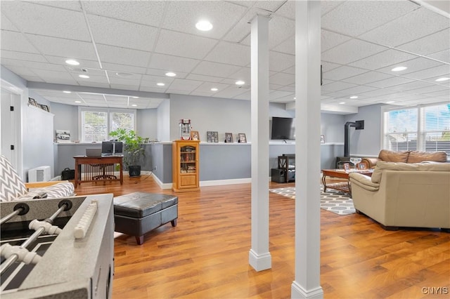 living room featuring light wood-style flooring, healthy amount of natural light, a paneled ceiling, and a wood stove