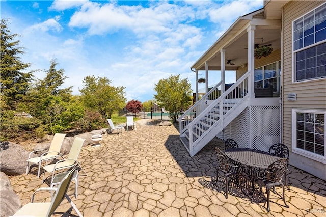 view of patio with a ceiling fan, stairs, fence, and outdoor dining space