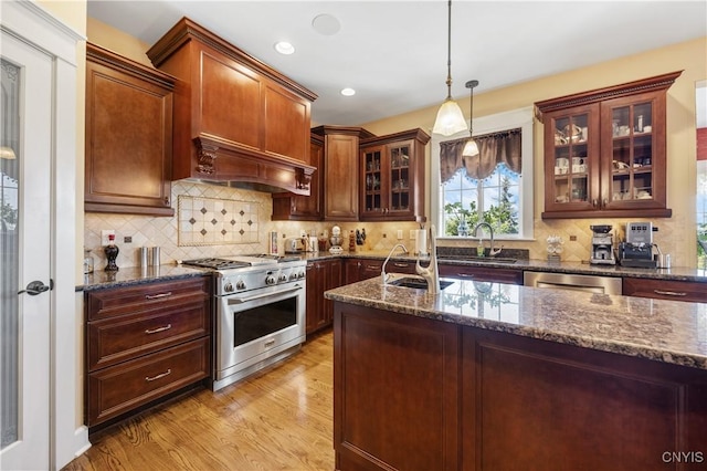 kitchen featuring stainless steel appliances, a sink, dark stone countertops, light wood-type flooring, and recessed lighting