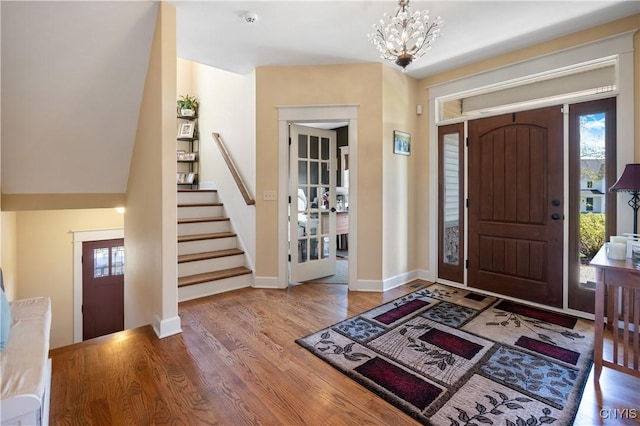 entrance foyer with stairs, wood finished floors, a chandelier, and baseboards