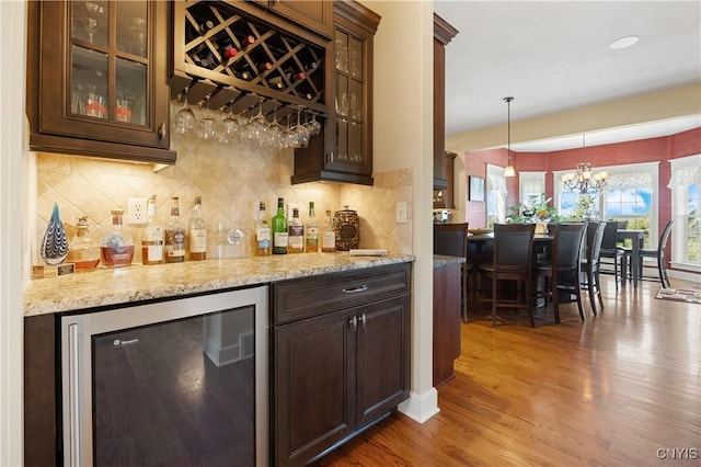 indoor dry bar with wine cooler, wood finished floors, a chandelier, backsplash, and pendant lighting