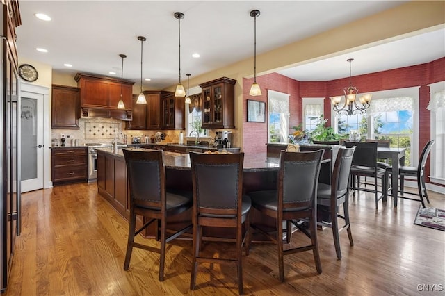 kitchen with a chandelier, glass insert cabinets, an island with sink, a breakfast bar area, and recessed lighting
