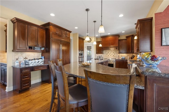 kitchen featuring wood finished floors, decorative backsplash, custom range hood, recessed lighting, and a kitchen bar