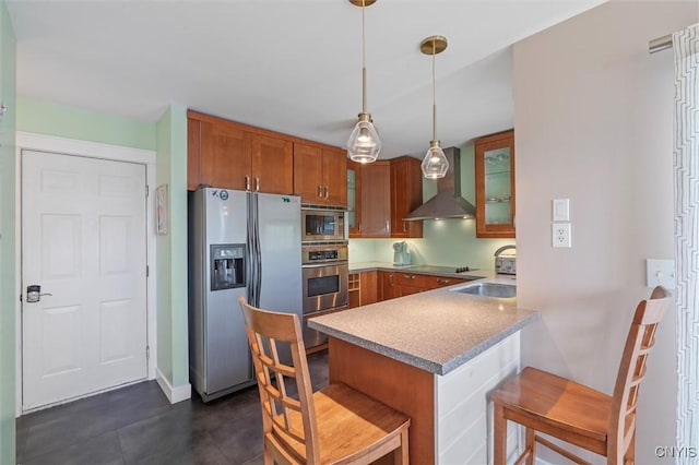 kitchen with appliances with stainless steel finishes, wall chimney exhaust hood, brown cabinetry, a peninsula, and glass insert cabinets