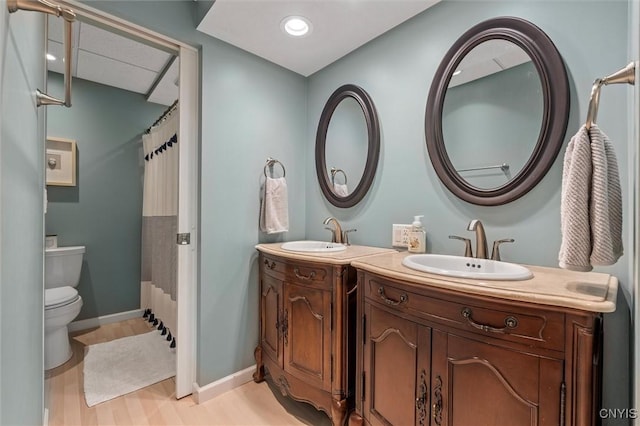 bathroom with two vanities, toilet, wood finished floors, and baseboards