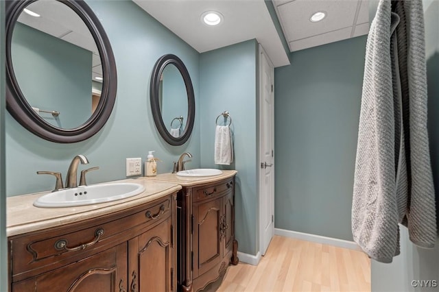 bathroom featuring wood finished floors, two vanities, baseboards, and recessed lighting