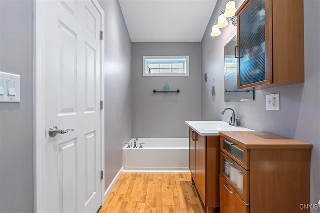 full bath featuring wood finished floors, a garden tub, vanity, and baseboards