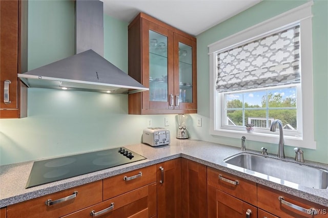 kitchen with wall chimney exhaust hood, black electric stovetop, a sink, glass insert cabinets, and brown cabinetry