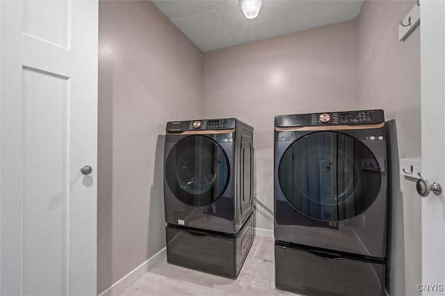 laundry room with washing machine and clothes dryer, baseboards, and light wood-type flooring