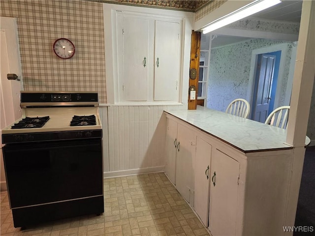 2282 Rte 305, Clarksville, NY 14727 - kitchen featuring gas stove, wallpapered walls, brick patterned floors, white cabinetry, and a peninsula