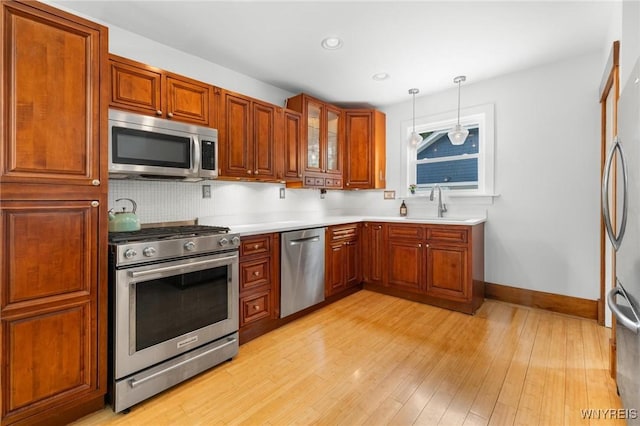 kitchen with appliances with stainless steel finishes, light wood-style floors, hanging light fixtures, baseboards, and light countertops
