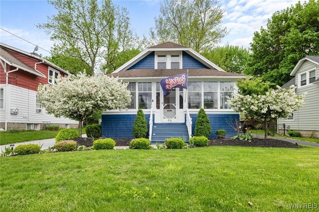 view of front of home featuring a front lawn, a shingled roof, and a sunroom