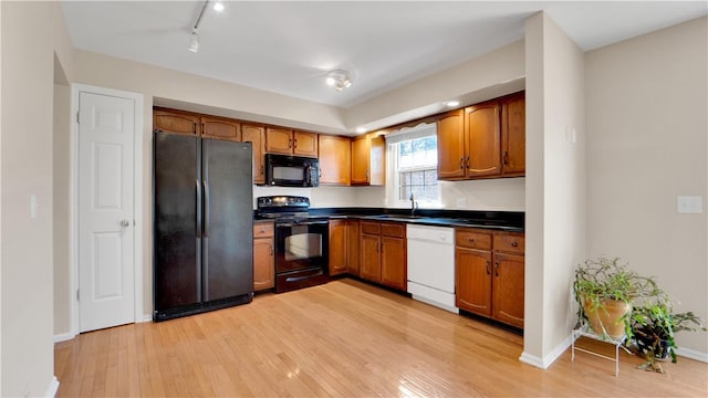 kitchen featuring black appliances, a sink, light wood-style floors, and dark countertops