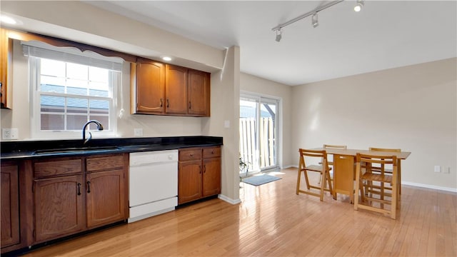 kitchen featuring dishwasher, a sink, dark countertops, light wood-style floors, and brown cabinetry