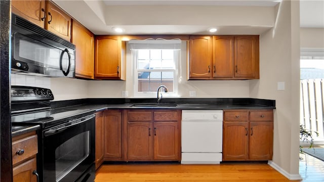 kitchen with black appliances, light wood finished floors, a sink, brown cabinetry, and dark countertops