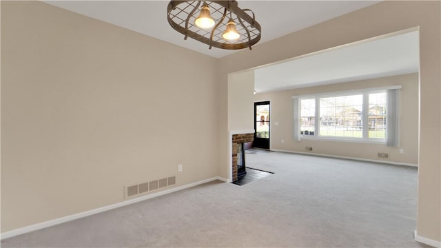 carpeted empty room with a fireplace with flush hearth, baseboards, and a chandelier