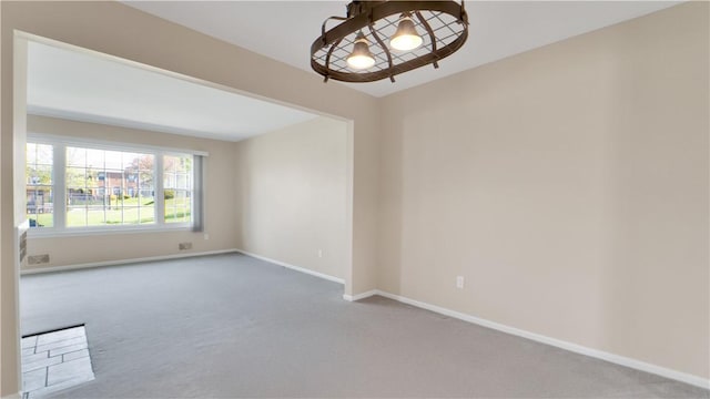 empty room featuring carpet floors, baseboards, and a chandelier