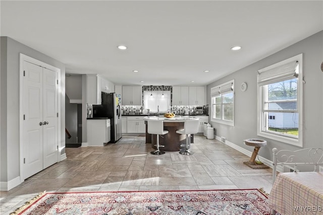 kitchen featuring baseboards, stainless steel fridge with ice dispenser, white cabinets, backsplash, and recessed lighting