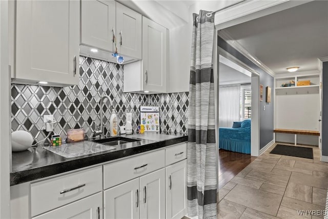 kitchen with a sink, white cabinets, backsplash, dark countertops, and crown molding