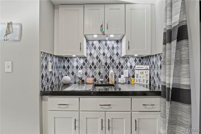 kitchen with dark countertops, white cabinetry, tasteful backsplash, and a sink