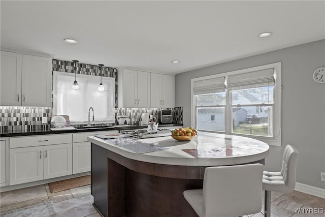 kitchen with a sink, decorative backsplash, white cabinets, a center island, and recessed lighting