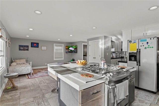 kitchen with appliances with stainless steel finishes, baseboards, a kitchen island, recessed lighting, and white cabinets