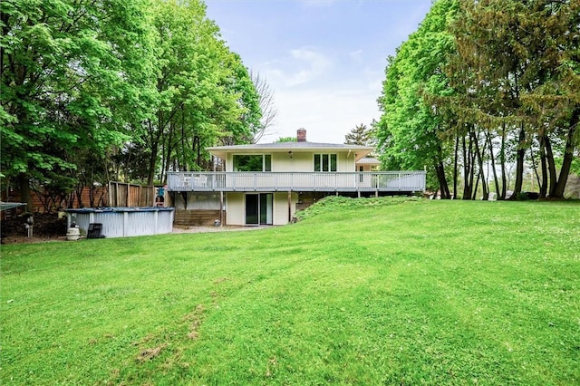 rear view of house featuring a chimney, a wooden deck, a lawn, and an outdoor pool