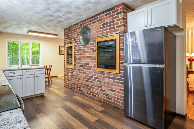kitchen with freestanding refrigerator, black oven, dark wood-style floors, white cabinetry, and light stone countertops