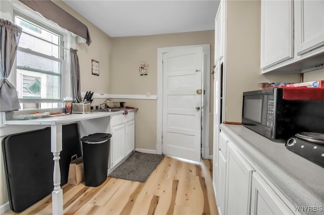2254 Grand Ave, Niagara Falls, NY 14301 - kitchen with black microwave, light wood finished floors, white cabinets, a sink, and baseboards