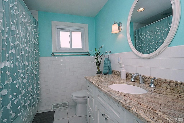 bathroom with tile walls, tile patterned floors, toilet, vanity, and wainscoting