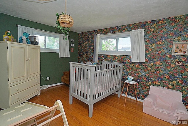 bedroom featuring wood finished floors, multiple windows, wallpapered walls, a textured ceiling, and baseboards
