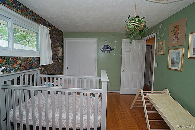 bedroom with wood finished floors, a closet, wallpapered walls, and a textured ceiling