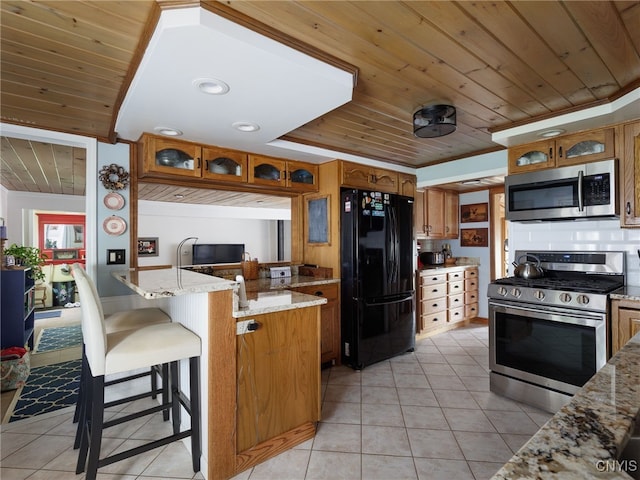 127 W St, Rutland, NY 13612 - kitchen with stainless steel appliances, wooden ceiling, brown cabinets, light tile patterned flooring, and light stone counters