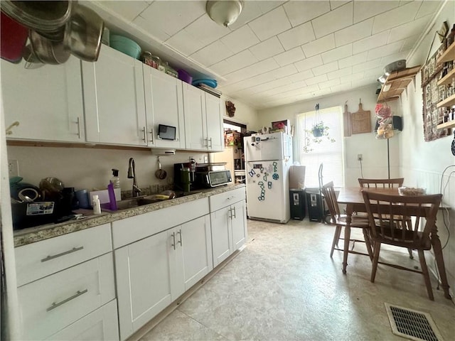 11 Gilbert St, Oneonta-City, NY 13820 - kitchen featuring freestanding refrigerator, a sink, white cabinetry, and light floors