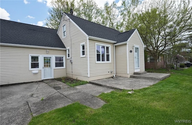 back of property with a yard, a patio area, and a shingled roof