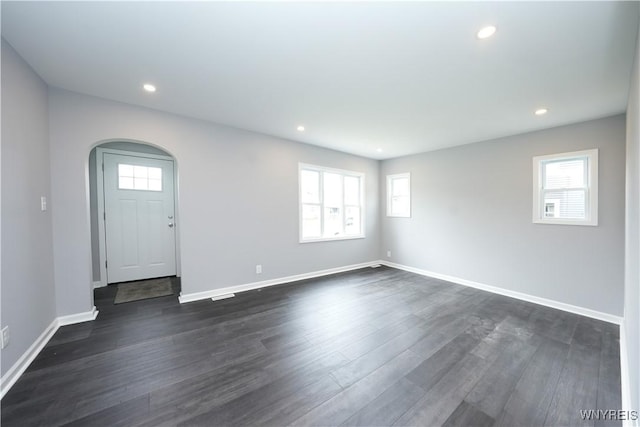 empty room with arched walkways, plenty of natural light, baseboards, recessed lighting, and dark wood-style floors