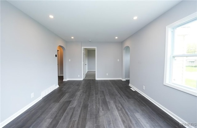 empty room with arched walkways, dark wood-style flooring, plenty of natural light, and recessed lighting