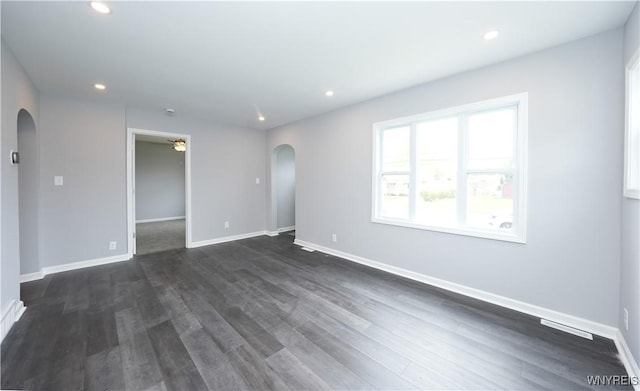 empty room featuring arched walkways, ceiling fan, recessed lighting, dark wood finished floors, and baseboards