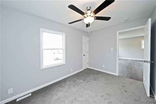unfurnished bedroom with baseboards, multiple windows, carpet flooring, and ceiling fan