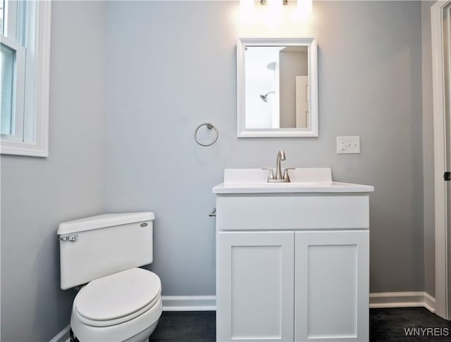 half bathroom with baseboards, vanity, and toilet