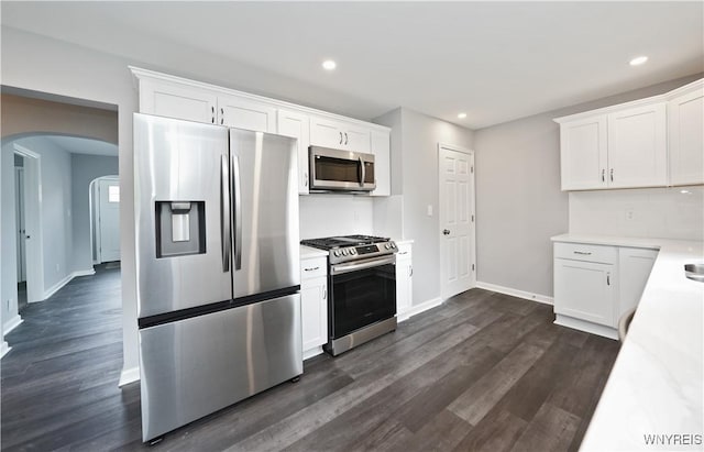 kitchen featuring appliances with stainless steel finishes, arched walkways, dark wood finished floors, baseboards, and light countertops