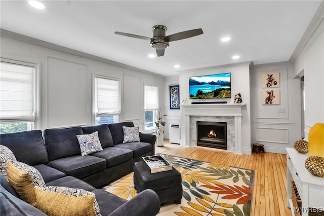 living room featuring ornamental molding, hardwood / wood-style floors, ceiling fan, a lit fireplace, and plenty of natural light