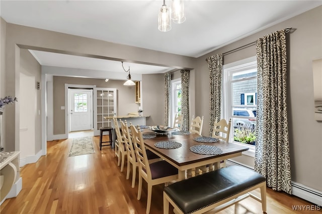 dining space featuring a baseboard heating unit, light wood finished floors, and baseboards