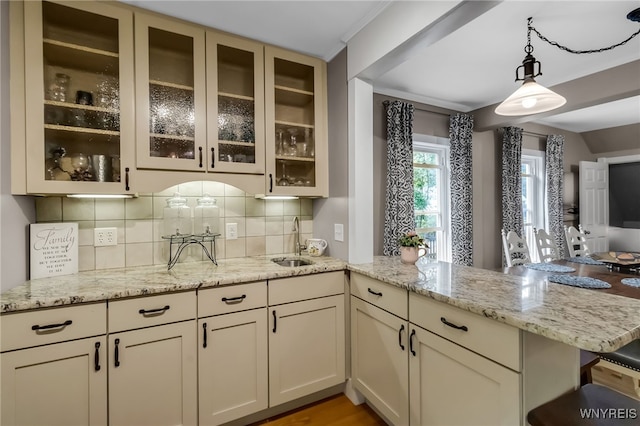 kitchen with a sink, a peninsula, light stone countertops, tasteful backsplash, and pendant lighting